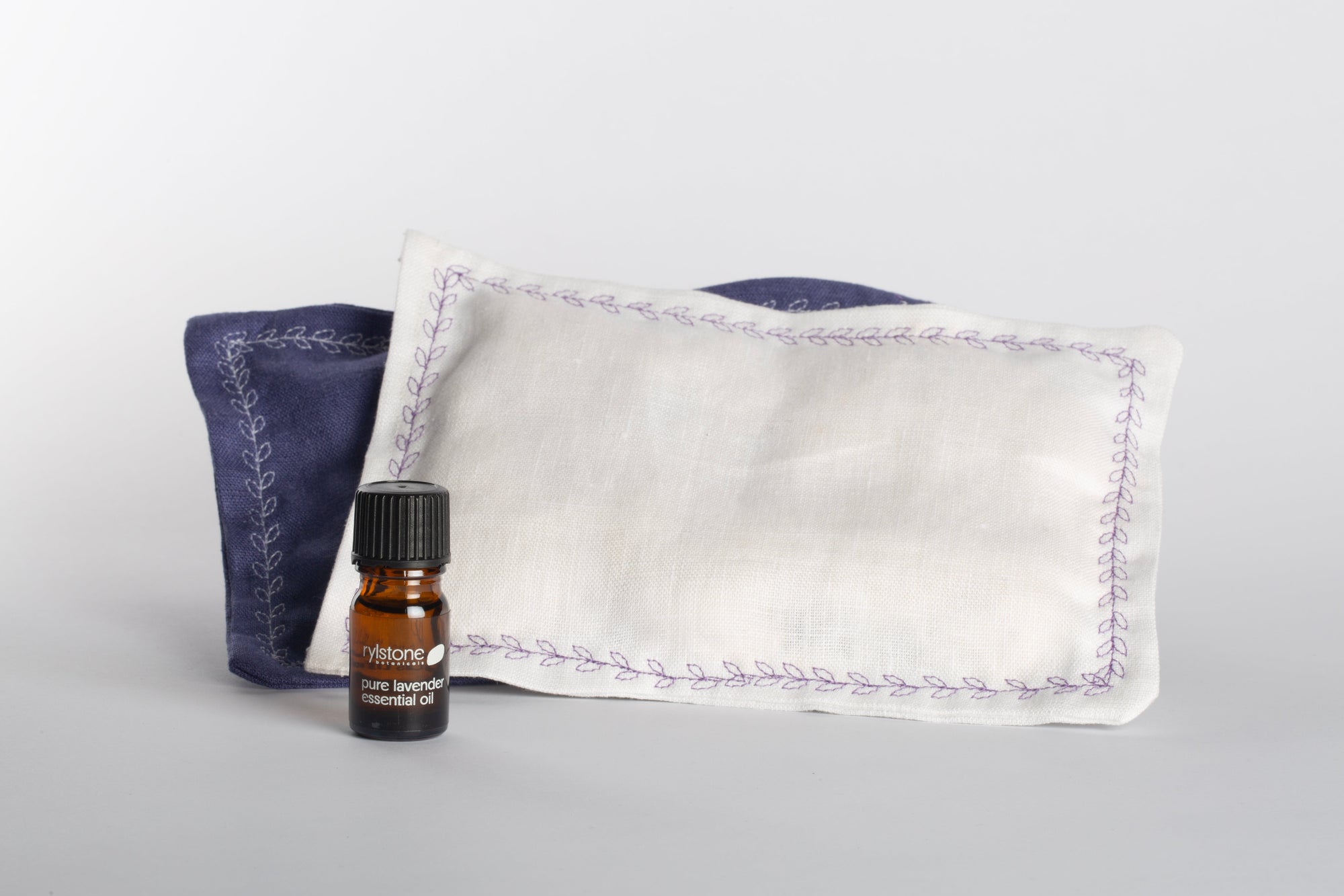 Small bottle of essential oil with two linen pillows, filled with lavender flowers and cotton.